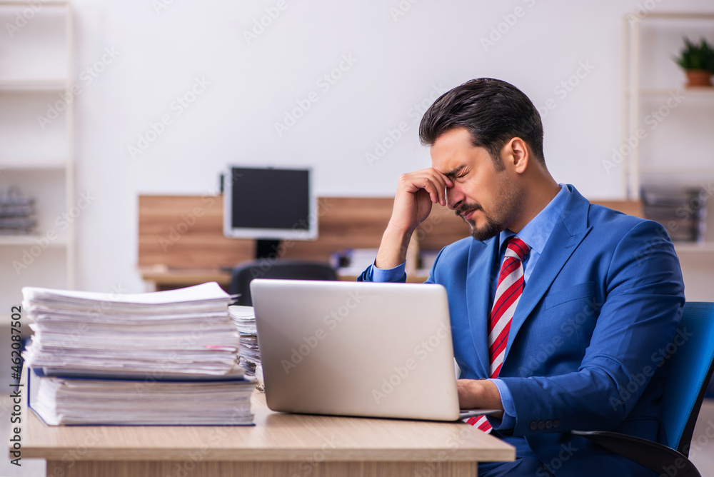 Young male employee unhappy with excessive work at workplace Young male employee unhappy with excessive work at workplace