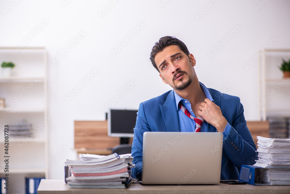 Young male employee unhappy with excessive work at workplace Young male employee unhappy with excessive work at workplace