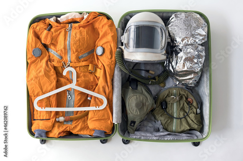 Murais de parede Open suitcase packed for space travelling with orange space suit, space helmet and space suit accessories on white background