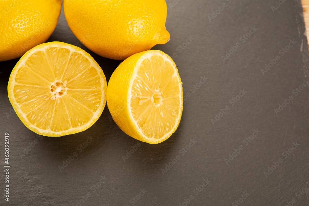 Whole lemon and lemon halved on slate plate and wooden background Whole lemon and lemon halved on slate plate and wooden background