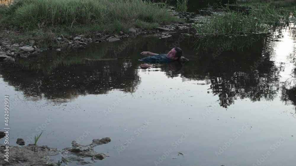 a man drowned , dead in the water , the body of a young man aged lies in the lake with his head on a stone, a corpse in a dirty pond unstable camera movement color correction. a man drowned , dead in the water , the body of a young man aged lies in the lake with his head on a stone, a corpse in a dirty pond unstable camera movement color correction.