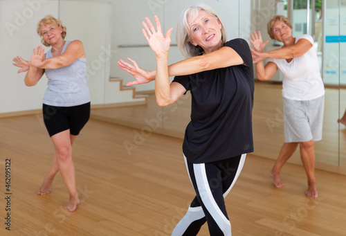 Portrait of smiling mature woman enjoying active dancing during group training in dance studio.