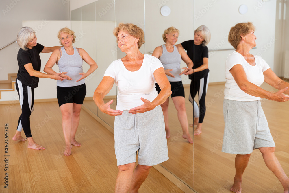 Positive senior women in sportswear dancing in fitness room. Their trainer helping them to learn new moves.
