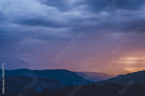 Atmospheric landscape with silhouettes of mountains on background of vivid dawn sky. Colorful nature scenery with sunset or sunrise of orange blue magenta violet pink lilac color. Sundown paysage.