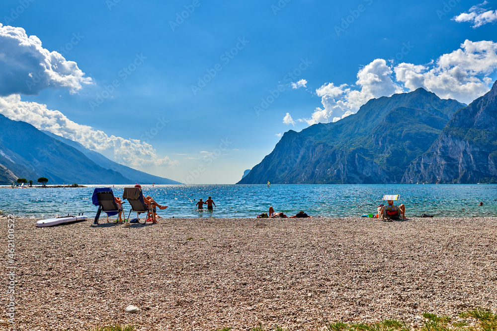 Torbole, Italy-09 October 2018: People sitting at the beach on the lounge chair and admiring Lake Garda in the summer time,View of the beautiful Lake Garda surrounded by mountains