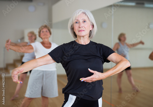 Portrait of positive mature woman practicing classic dance moves during group class in studio.