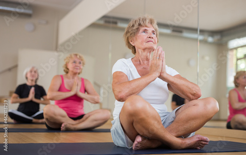 Mature women in sportswear exercising lotus pose together during group yoga class.