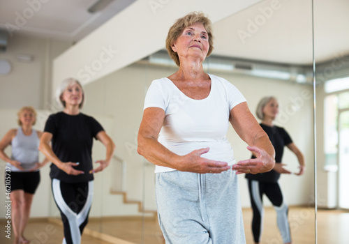 Positive senior women in sportswear dancing ballet in fitness room.