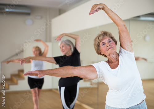Portrait of interested senior lady learning classic dance moves during group class in studio.