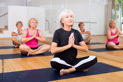 Group of mature women are doing yoga, sitting in the lotus position in a fitness studio