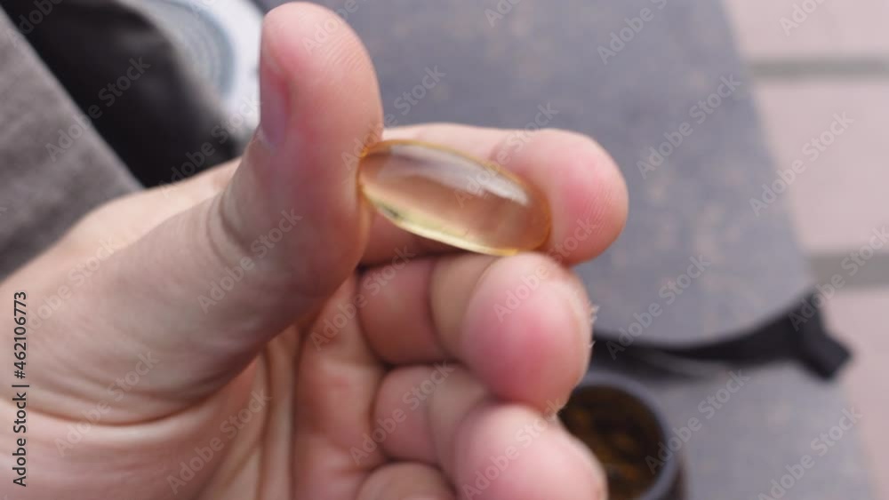 Person hand holds and spins clear yellow liquid medicine capsule in fingers over drug bottle against blurry background extreme closeup