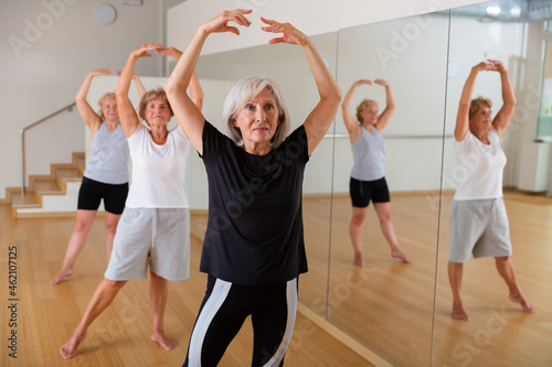 Active mature woman visiting choreography class with group of aged females, learning classical ballet technique .