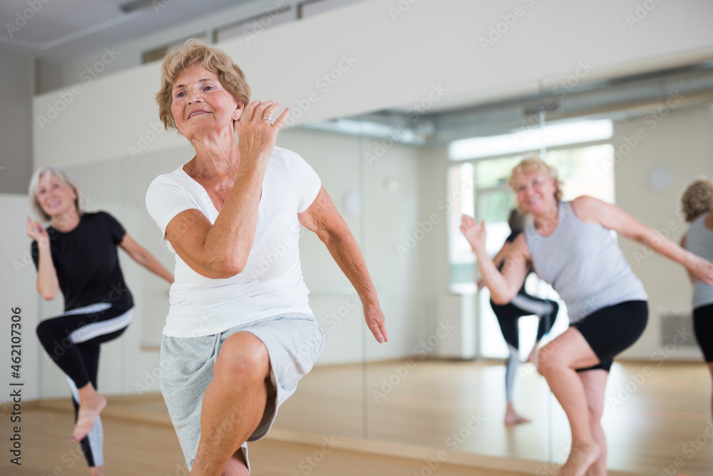 Fototapeta premium Portrait of mature energetic woman and people practicing active dancing in the studio at a group lesson