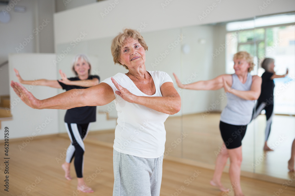 Portrait of mature energetic woman and people practicing active dancing in the studio at a group lesson