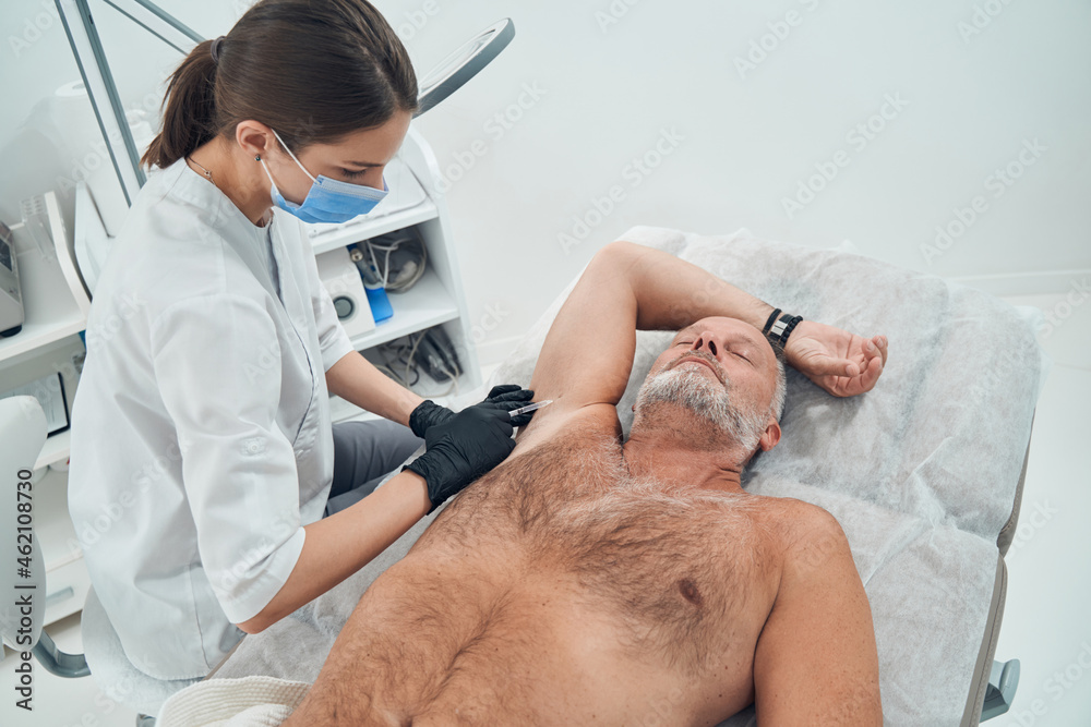 Male person receiving underarm injection in cosmetology clinic Male person receiving underarm injection in cosmetology clinic
