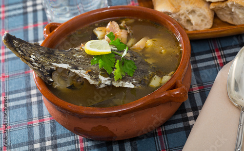 Delicious fish broth with sturgeon served in clayware with greens and lemon slice.. photo