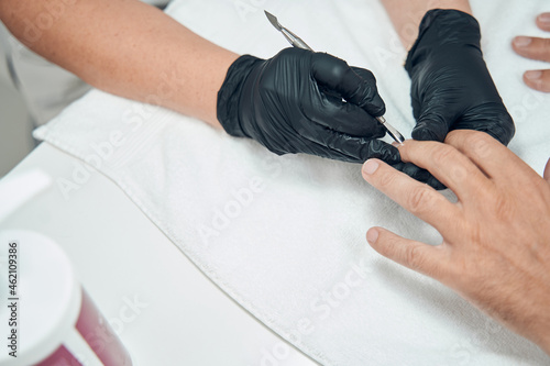 Manicurist removing cuticle on man finger with metal tool