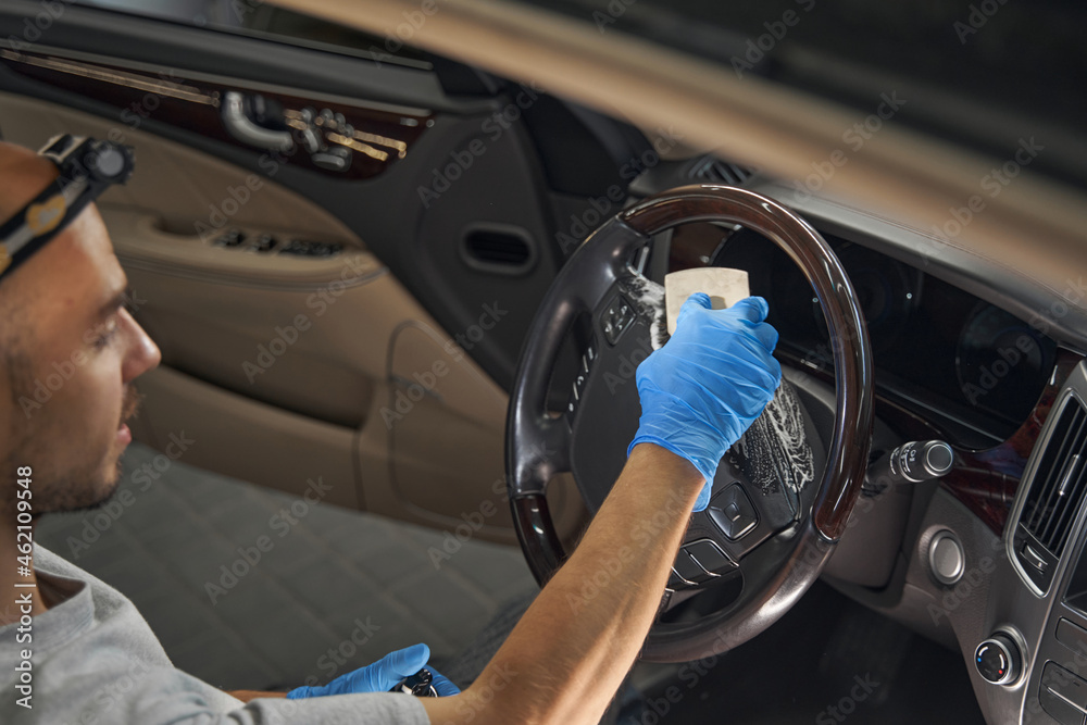 Car wash worker polishing vehicle steering wheel in garage
