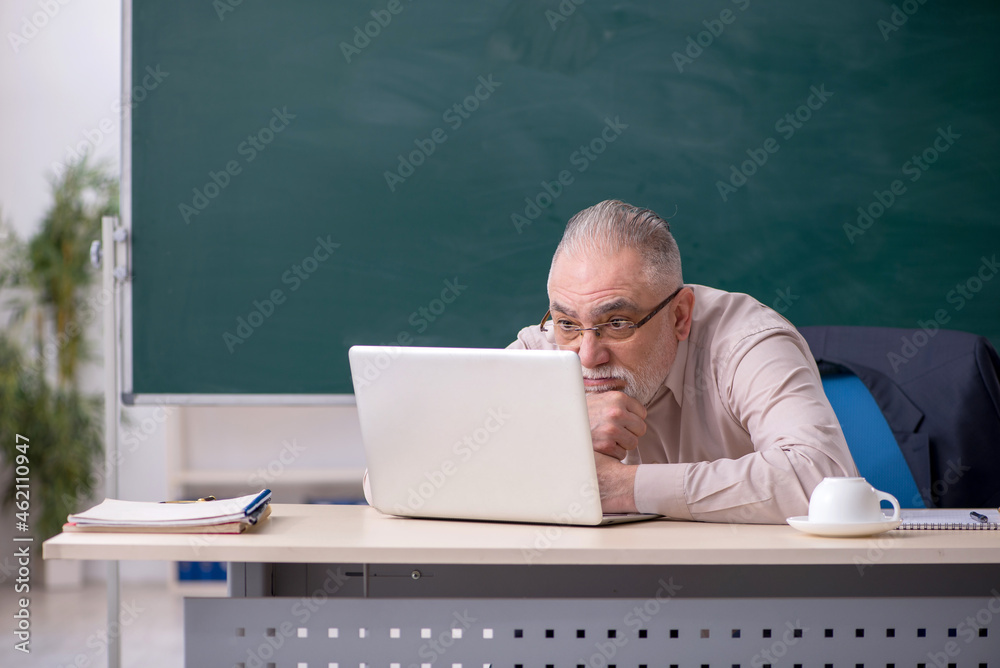 Old male teacher in front of blackboard Old male teacher in front of blackboard