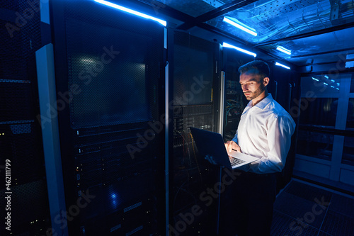 Fotografia Professional system administrator clicking on laptop near server cabinets
