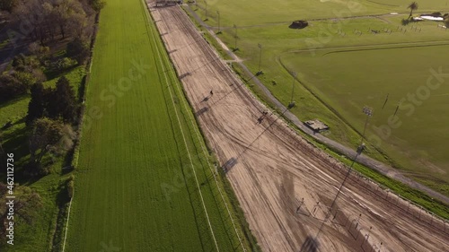 Aerial shot of two race horses walking on sandy racecourse track during training session for race photo