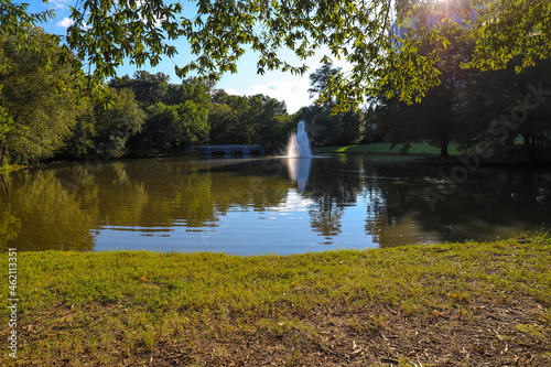 a gorgeous shot of the silky green lake water with a fountain in the middle of the lake with a stone bridge surrounded by lush green and autumn colored trees at Lenox Park in Brookhaven Georgia USA photo