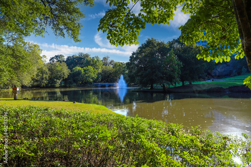 a gorgeous shot of the silky green lake water with a fountain in the middle of the lake with a stone bridge surrounded by lush green and autumn colored trees at Lenox Park in Brookhaven Georgia USA photo