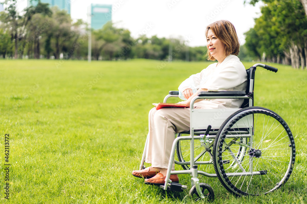 Fototapeta premium Senior adult elderly asia women sit on wheelchair and reading book outdoor