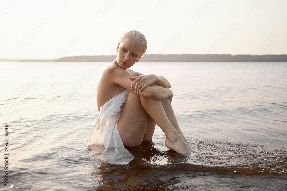 Art nude sexy blonde with short haircut is sitting in water on shore ...