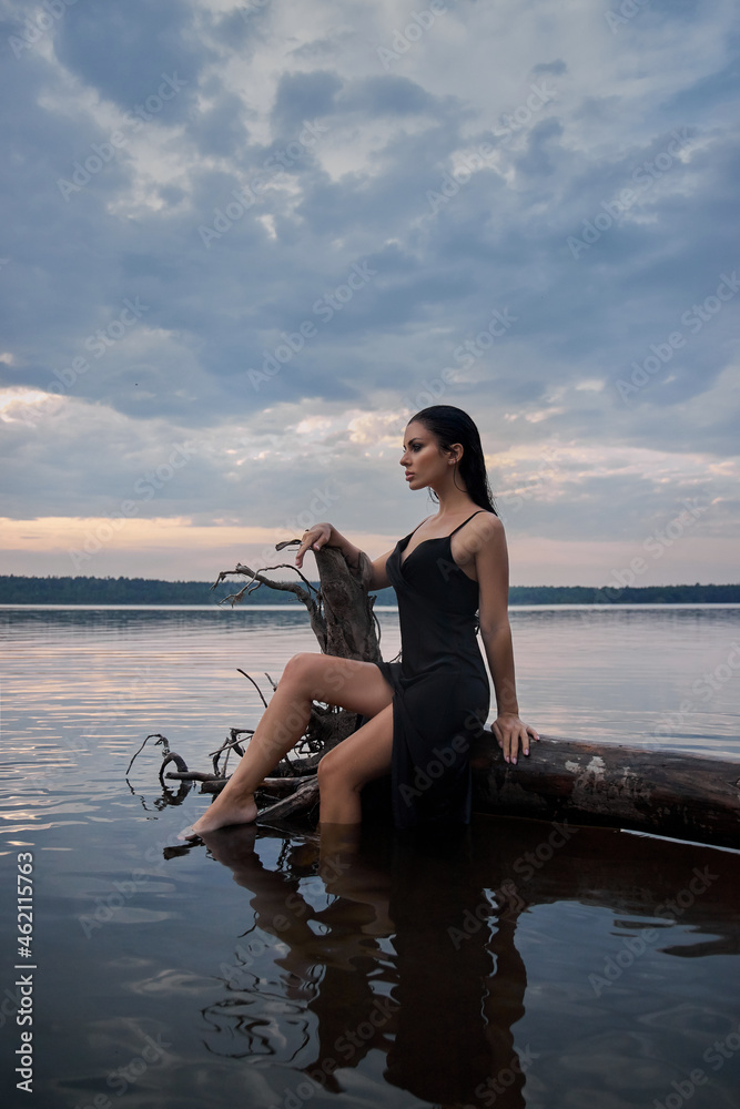 Beauty brunette woman in a black dress poses in a sea lake against a blue sky background. Long hair sexy woman and beautiful beauty makeup on her face Beauty brunette woman in a black dress poses in a sea lake against a blue sky background. Long hair sexy woman and beautiful beauty makeup on her face
