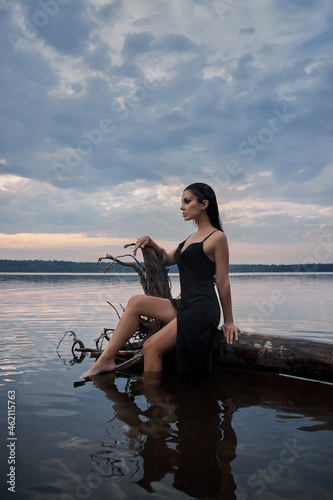 Beauty brunette woman in a black dress poses in a sea lake against a blue sky background. Long hair sexy woman and beautiful beauty makeup on her face © angel_nt