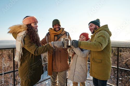 Obraz na plátně Cheerful friends clinking with mugs of hot tea while spending winter day in natu