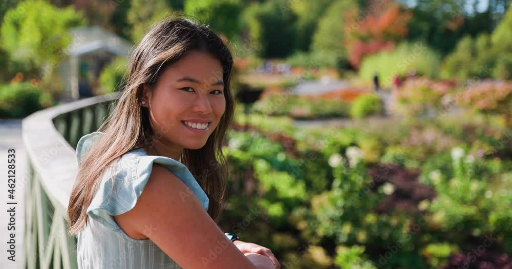 Beautiful Asian woman looking towards camera and smiling in beautiful vibrant park Beautiful Asian woman looking towards camera and smiling in beautiful vibrant park