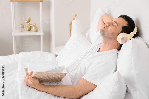Young man with book listening to music in bedroom