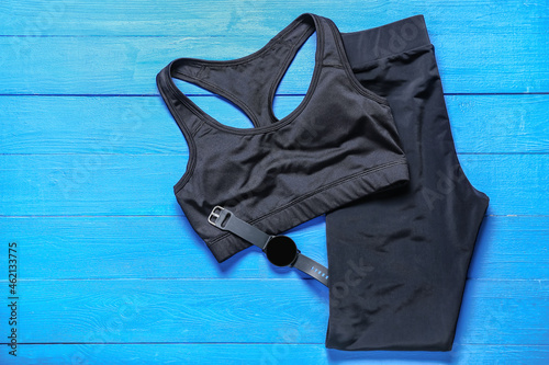 Sportswear and smartwatch on color wooden background