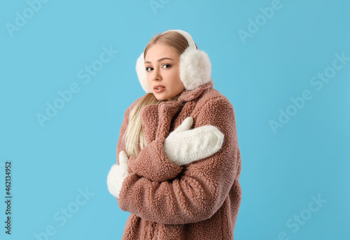 Frozen woman in winter clothes, mittens and fur earmuffs on blue background