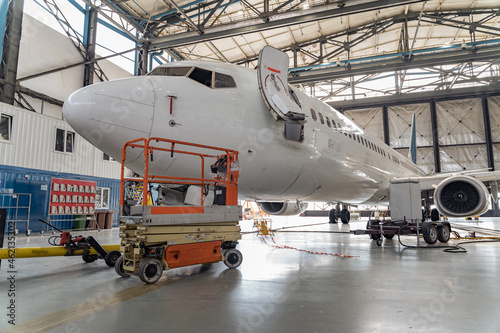 Big white passenger airplane on maintenance repair check in airport hangar indoors. Aircraft concept