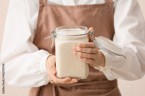 Woman holding glass jar of fresh sourdough on light background, closeup