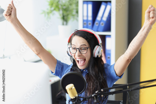 Joyful enthusiastic presenter in headphones with microphone looks at computer monitor. Sports commentator photo
