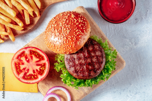 Hamburger ingredients, shot from above with French fries and ketchup, on a rustic wooden board