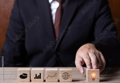 businessman holding finger point at lightbulb wooden block goal target plan for business with teade graph. copy space for text.