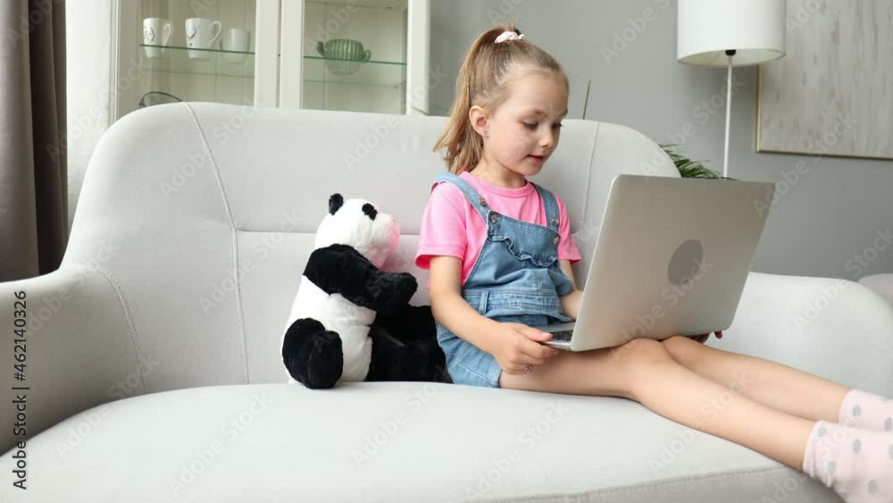 Distance learning. Cheerful little girl using laptop computer studying through online e-learning system.