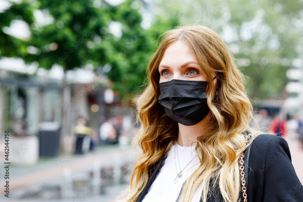 Portrait of young beautiful woman wearing medical mask as protection against corona virus. Covid pandemic time in Europe and in the world. Safety for people. Woman in summer city.
