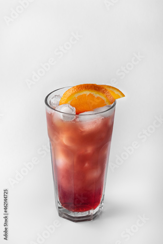 beautiful transparent glass of summer drink. red and yellow lemonade with ice and orange isolated on a white background with natural shadows