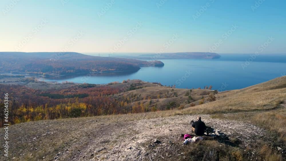 Cinematic aerial view of a beautiful autumn forest with golden foliage, mountain scenery and a lone traveler relaxing sitting on a stone. Dramatic drone shooting in UHD 4K resolution. Cinematic aerial view of a beautiful autumn forest with golden foliage, mountain scenery and a lone traveler relaxing sitting on a stone. Dramatic drone shooting in UHD 4K resolution.