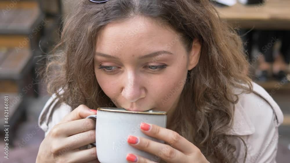 Young woman with long loose hair and bright manicure tastes capuccino from big porcelain cup and smiles at break in cafe closeup Young woman with long loose hair and bright manicure tastes capuccino from big porcelain cup and smiles at break in cafe closeup