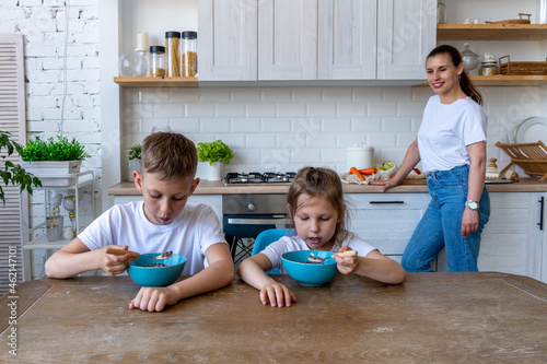 Two children are sitting table in the kitchen eating breakfast.