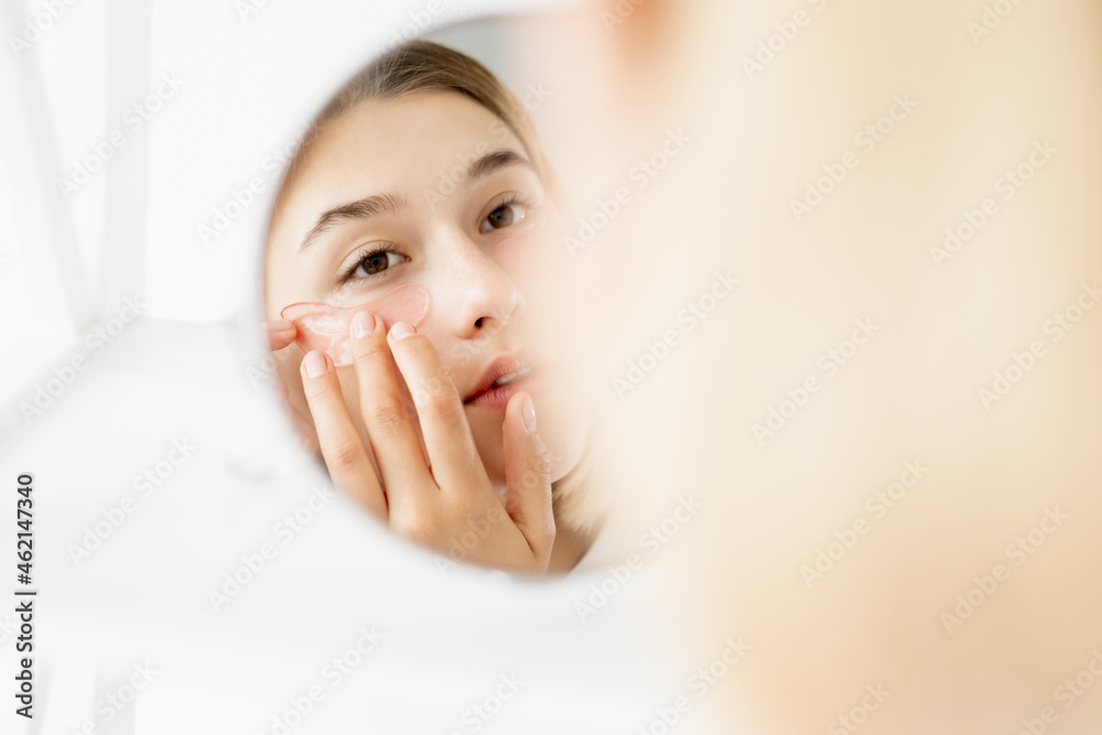Under eye moisturizing. Beauty care. Collagen pads. Attractive young woman applying hydrogel recovery patches at mirror on white background. Under eye moisturizing. Beauty care. Collagen pads. Attractive young woman applying hydrogel recovery patches at mirror on white background.