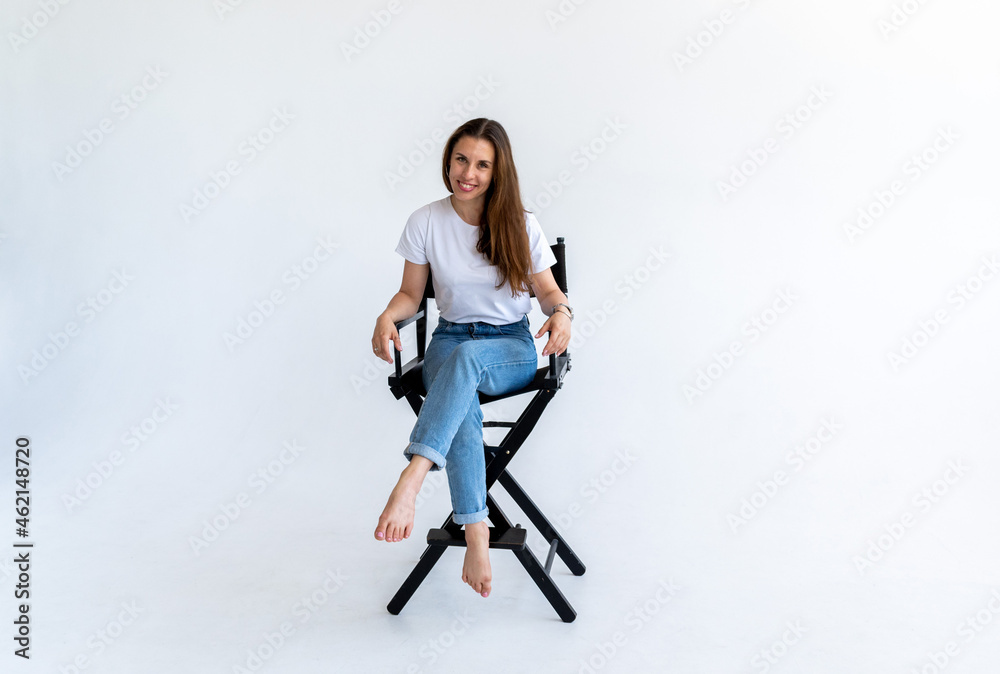 Adult woman sits on a filmmaker's chair in blue jeans and a white T-shirt. Adult woman sits on a filmmaker's chair in blue jeans and a white T-shirt.