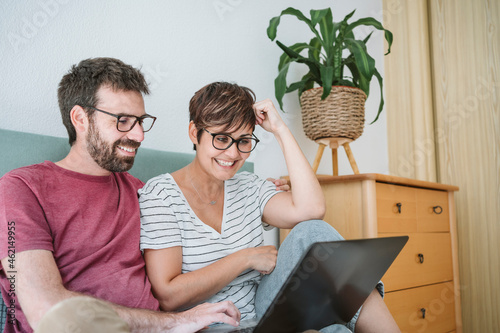 Smiling mid adult couple using laptop while sitting on bed